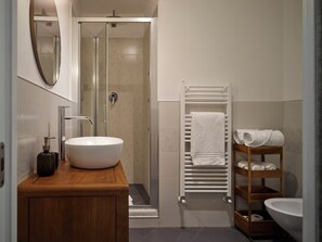 A modern bathroom with a wooden vanity, a white sink, a glass shower enclosure, a white towel rack, and a wooden shelf with towels. - La Residenza dell'Orafo (Florence)