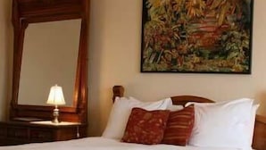 A neatly made bed with white linens and two pillows, a wooden headboard, a nightstand with a lamp, and a large mirror.
