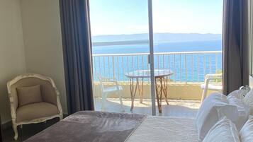 Une chambre d’hôtel avec un lit, une chaise, une petite table et un balcon donnant sur la mer.