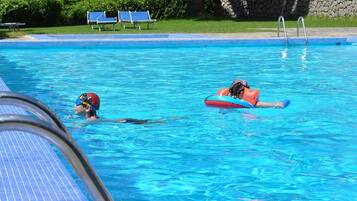 Une piscine à l’eau d’un bleu cristallin, un plongeoir et, au fond, des chaises longues.