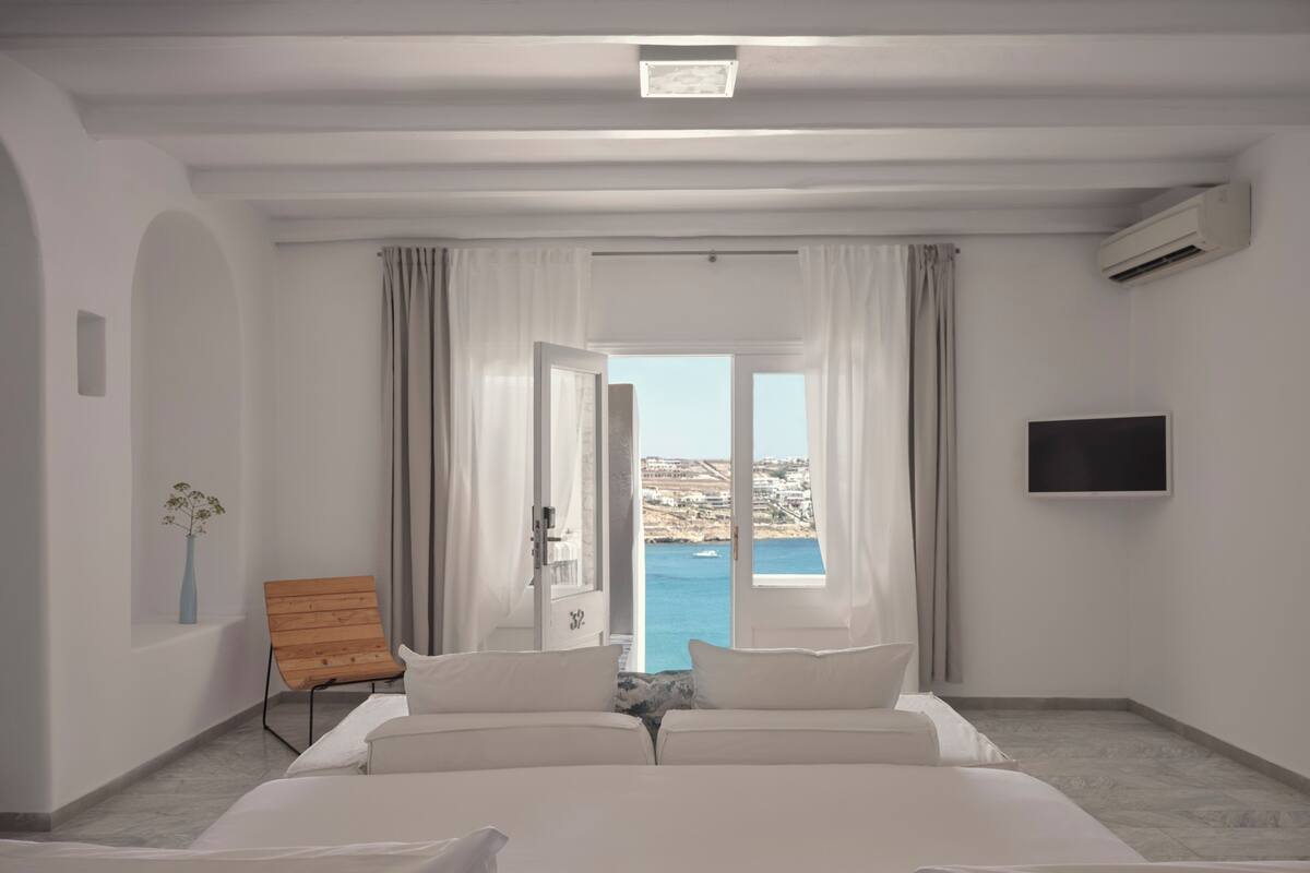 Habitación de hotel con cama, televisión, una silla de madera y vista al mar.