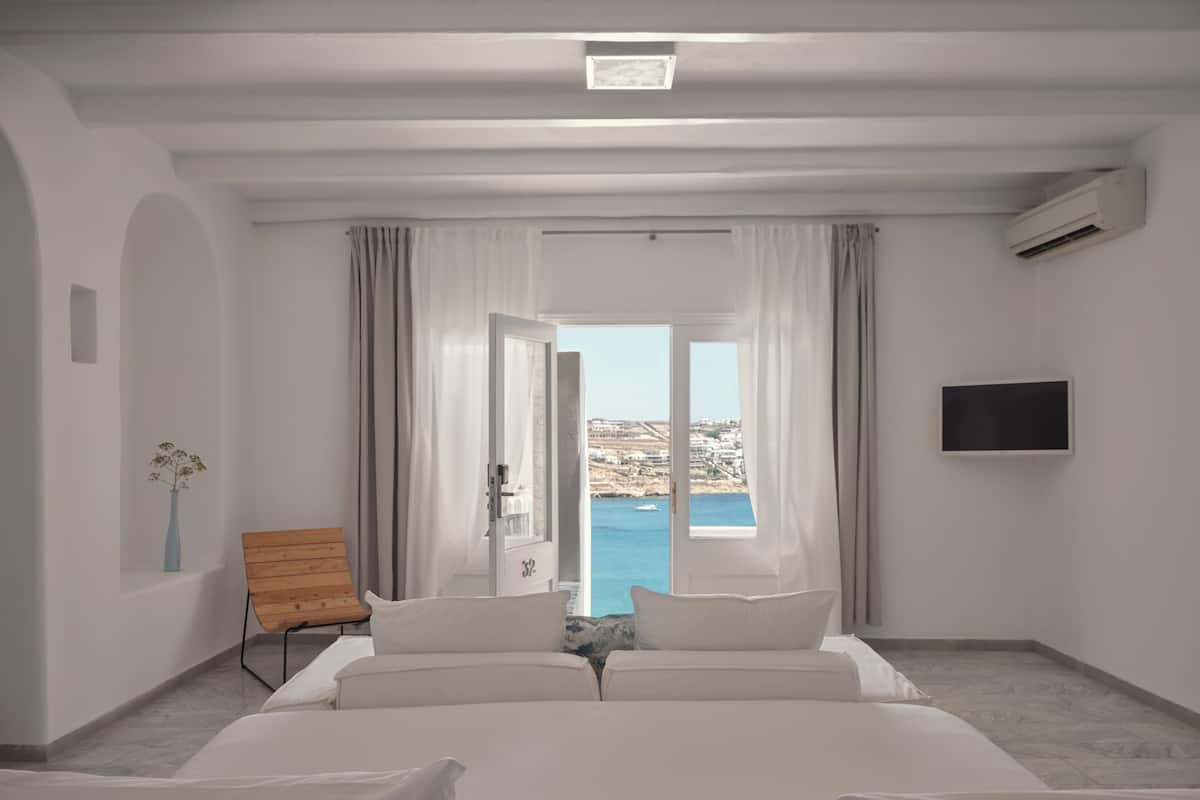 Ein Hotelzimmer mit Bett, Fernseher, Holzstuhl und Meerblick.