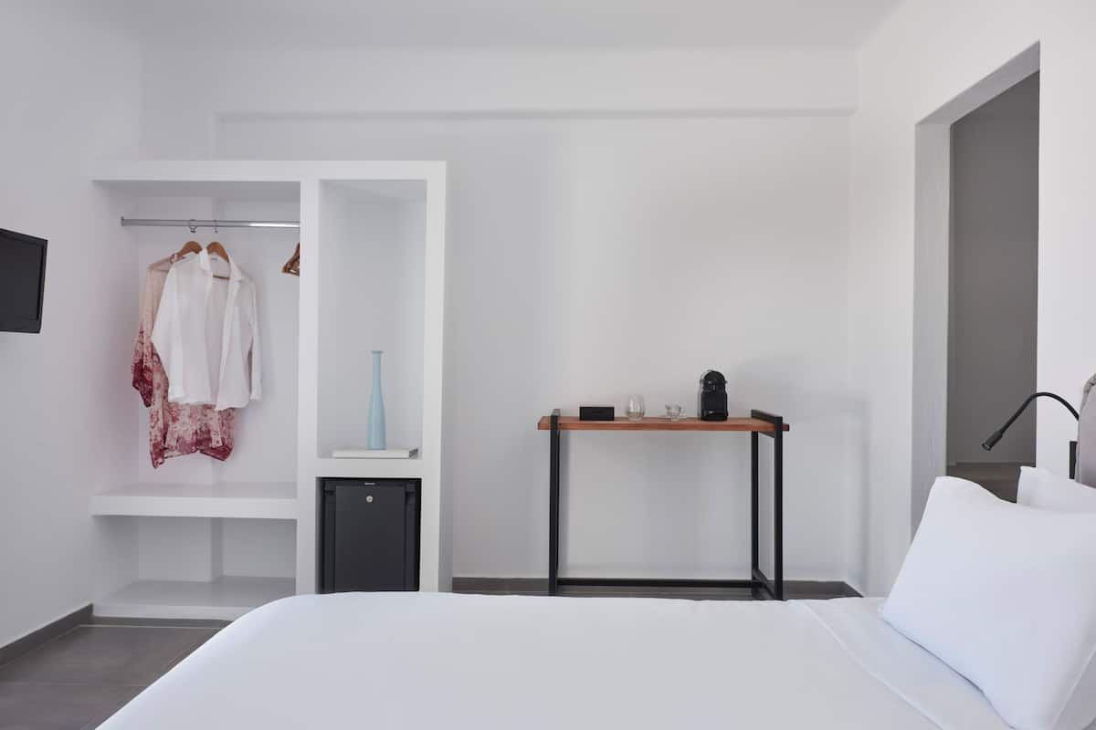 Habitación de hotel moderna con cama, armario, una mesita de noche con lámpara y escritorio con cafetera.