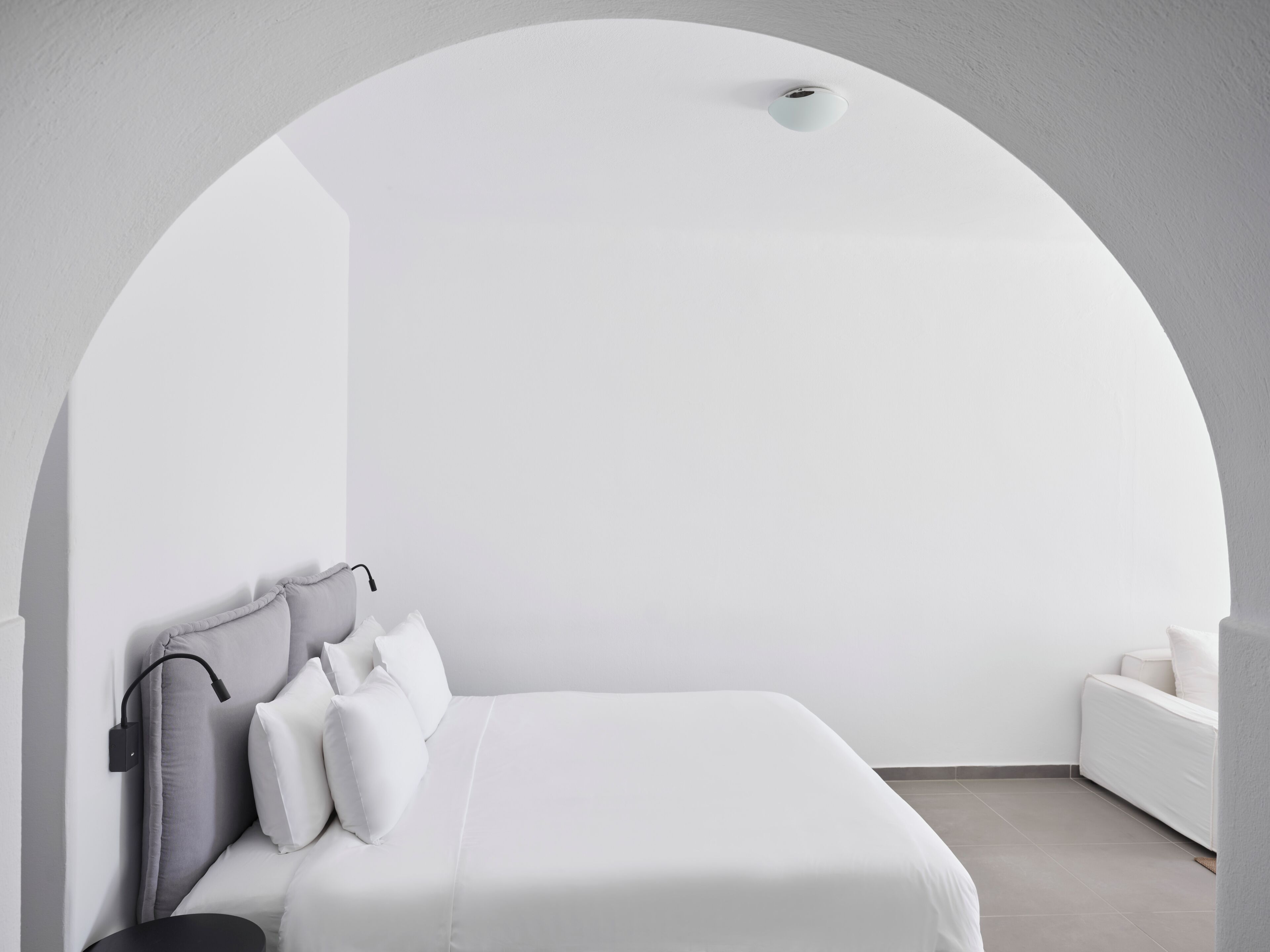 A minimalist bedroom with a white bed, grey pillows, a black side table, and a white nightstand.