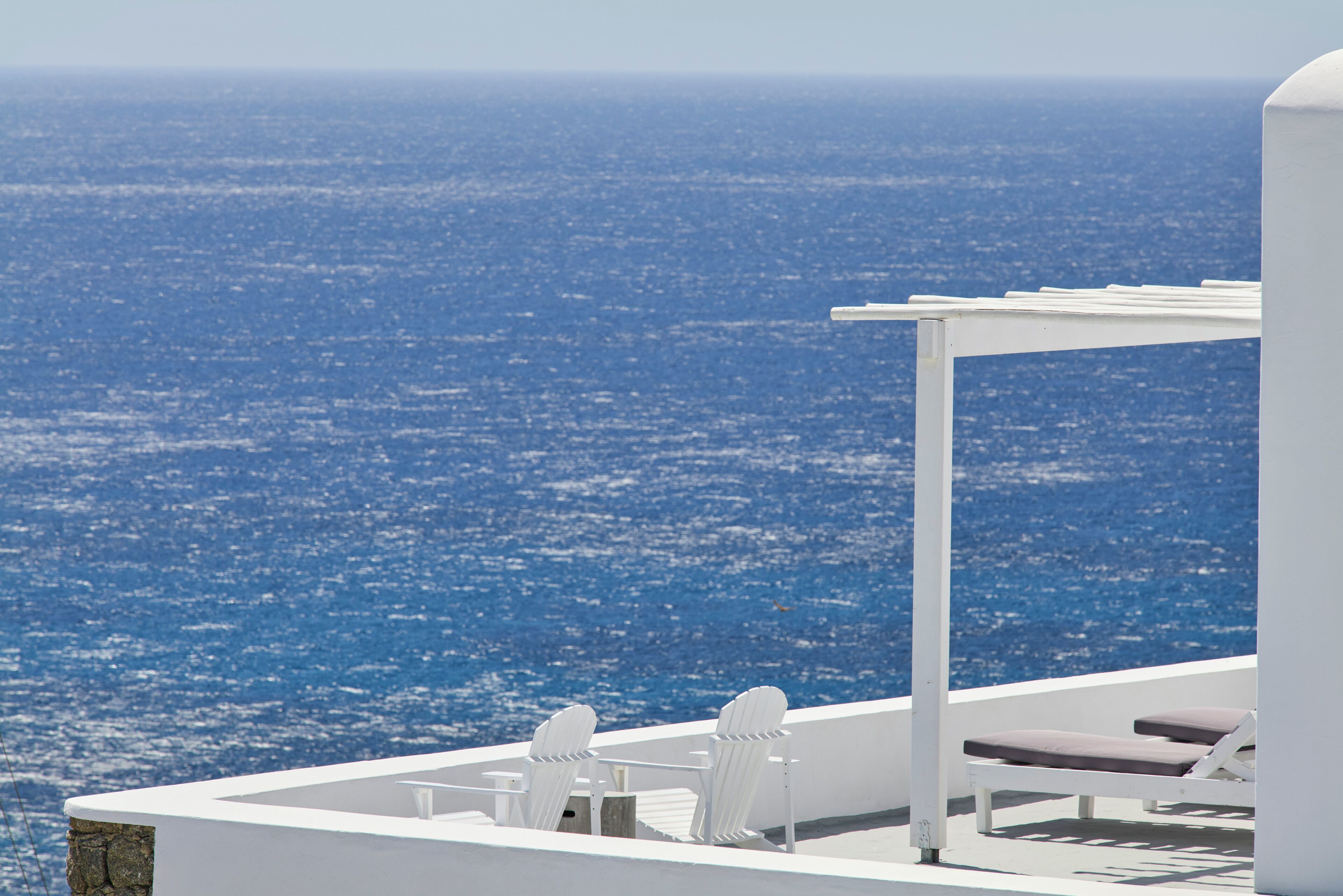 A white outdoor seating area with a view of the ocean and cityscape.