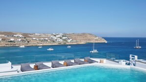 A pool with lounge chairs, a clear view of the sea, and a distant coastal village. - Pietra e Mare - Mykonos Moments by Mr and Mrs White (Mykonos)