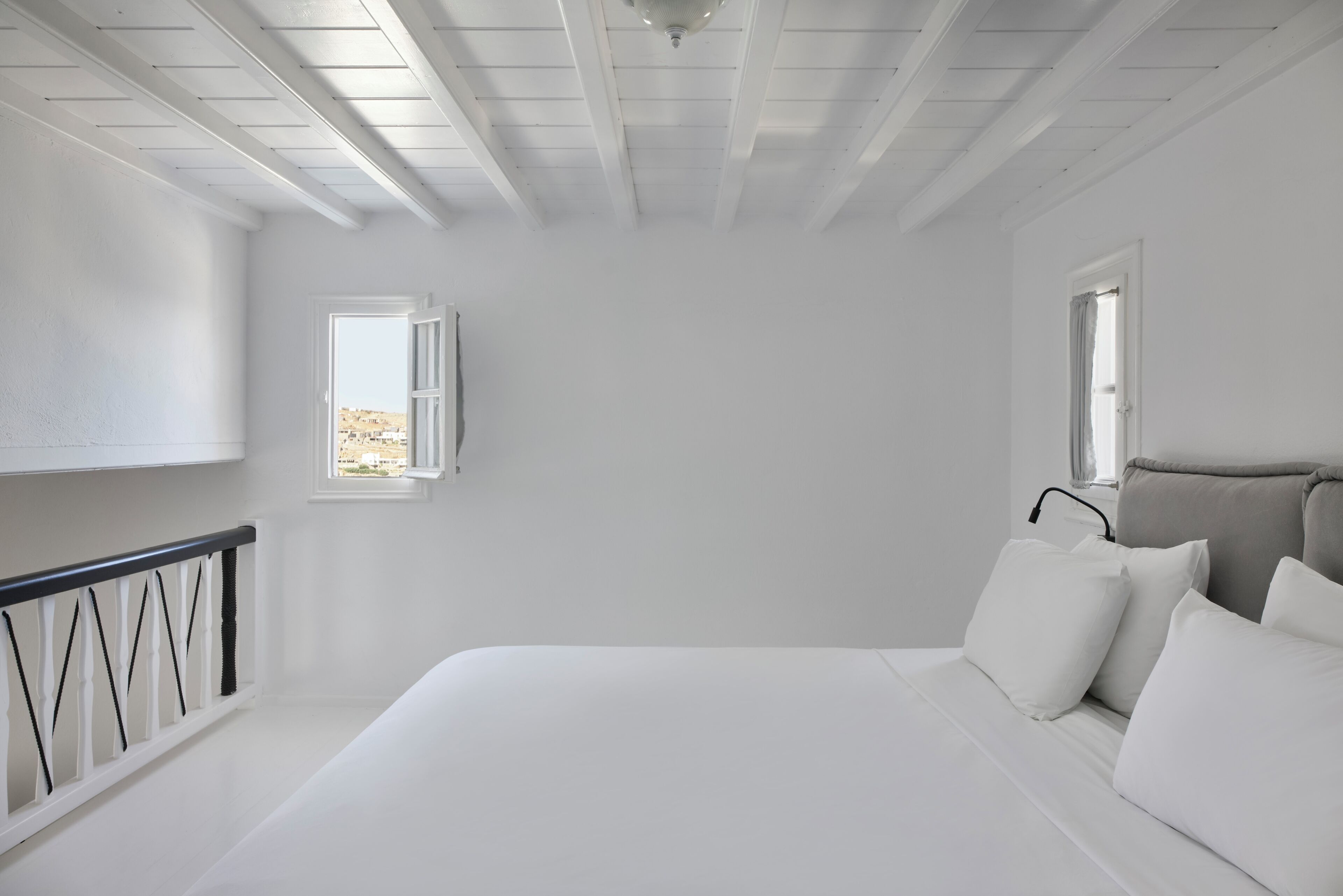 A bedroom with a bed, a window, and a balcony railing.