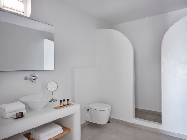 A modern bathroom with a white sink, mirror, and toilet. There is a wooden shelf with towels and toiletries. - Pietra e Mare - Mykonos Moments by Mr and Mrs White (Mykonos)