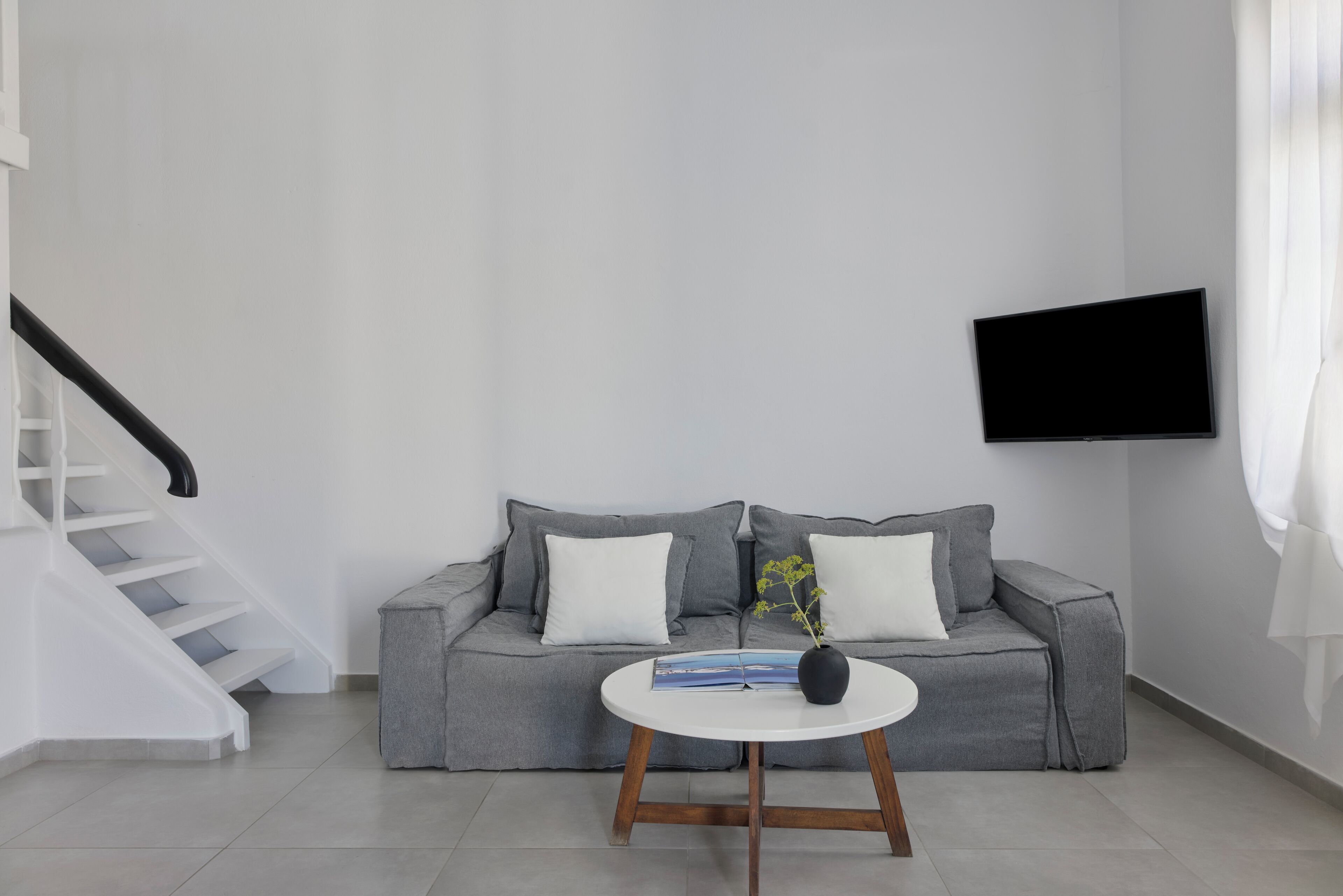 En moderne stue med en grå sofa, et hvidt sofabord, en sort vase og et fladskærms-TV monteret på væggen.