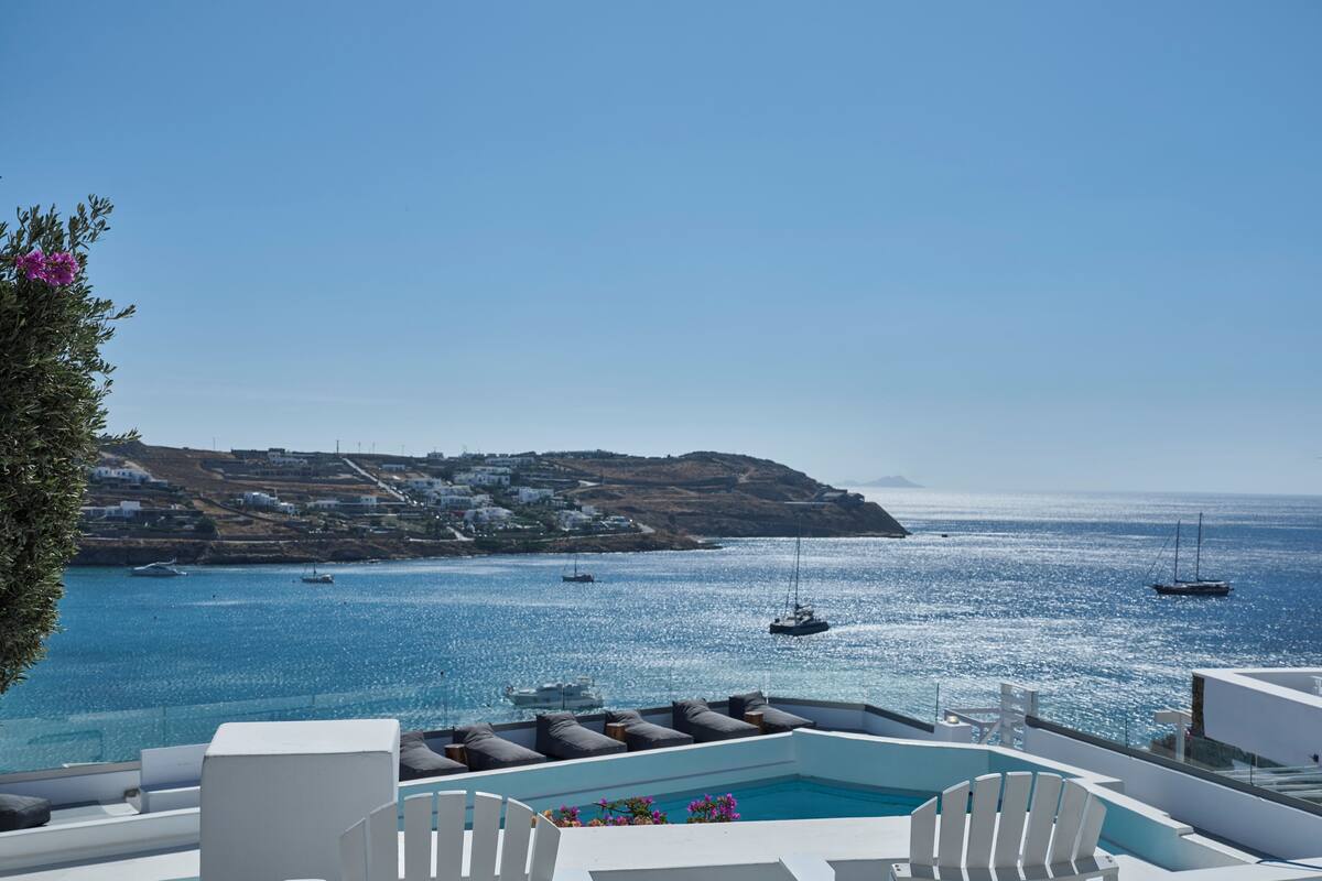 Zona junto a la piscina con mobiliario blanco, vista al mar y barcos.