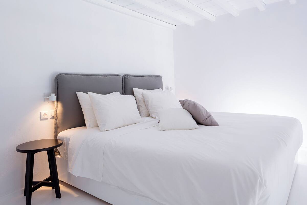 Un dormitorio moderno con una cama, almohadas, una mesita de noche y una lámpara fijada a la pared.