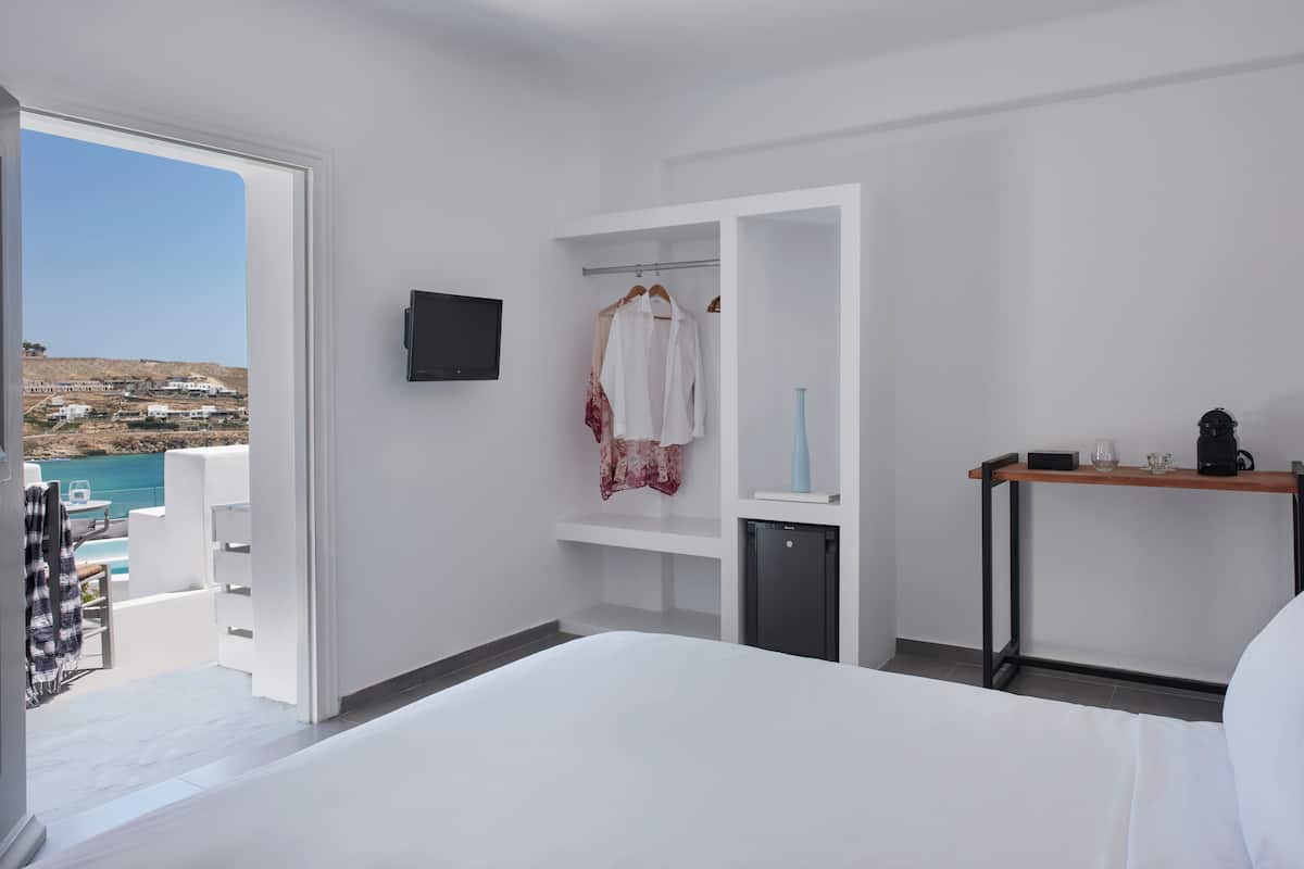 Habitación de hotel con cama, televisión, escritorio con cafetera, un mueble pequeño y vista al mar.