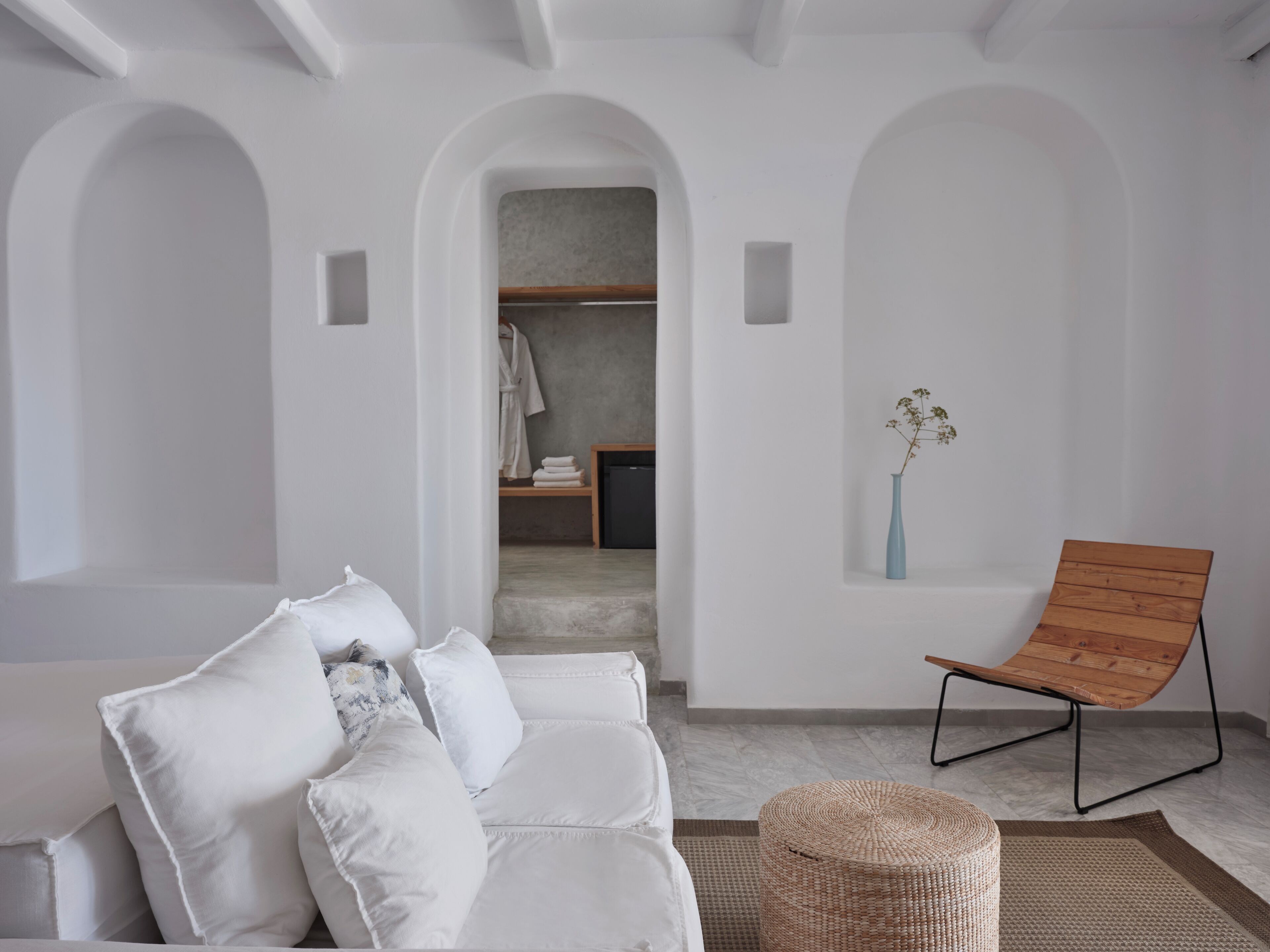 A modern interior with a white sofa, a wooden chair, and a wicker ottoman.