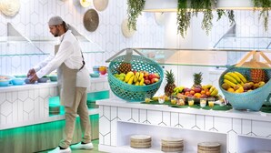 A modern kitchen with a chef preparing food, two large baskets of fresh fruits, and neatly stacked plates on shelves. - HD Parque Cristobal Tenerife (Arona)