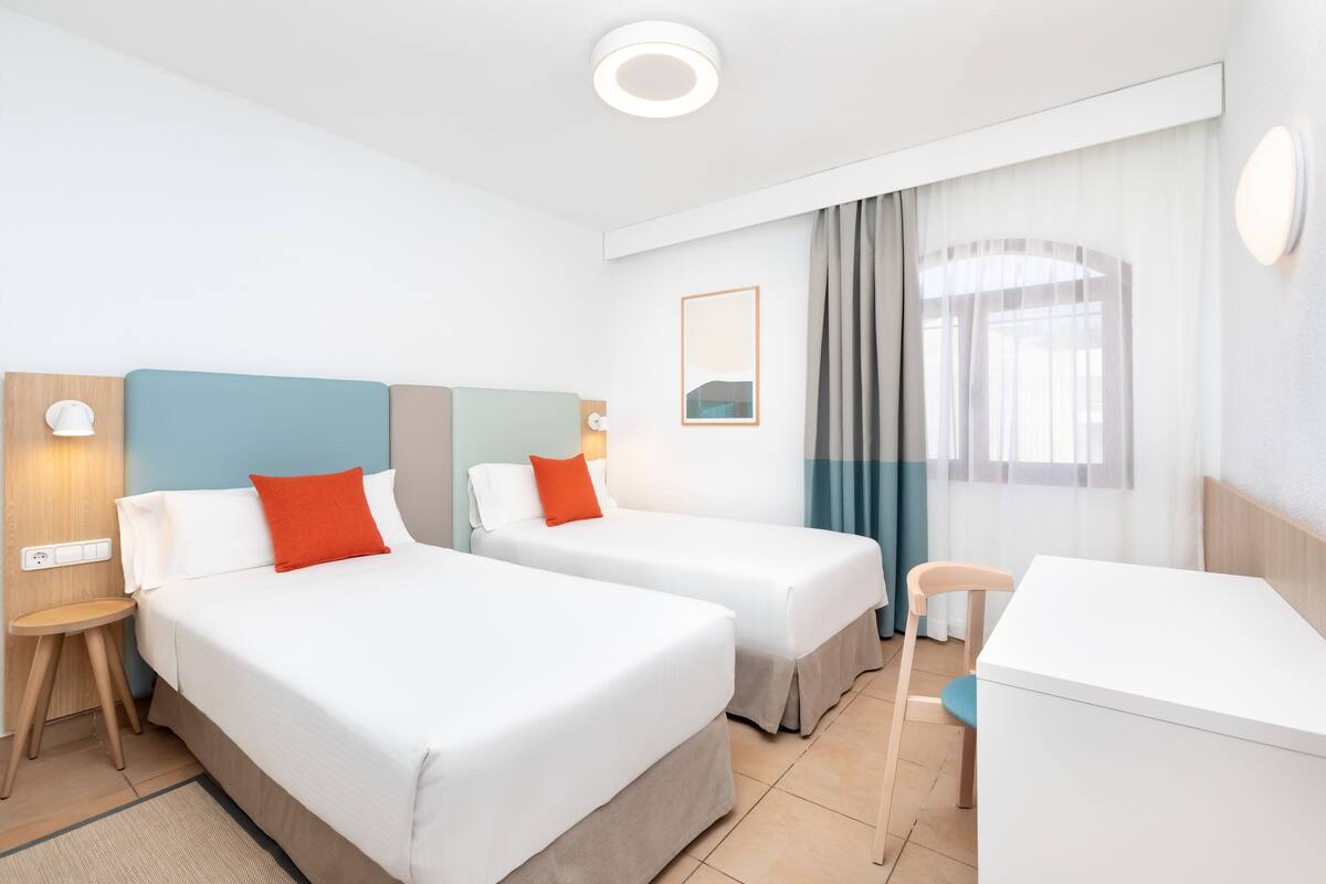 Une chambre d’hôtel avec deux lits, un bureau, une chaise et une petite table.