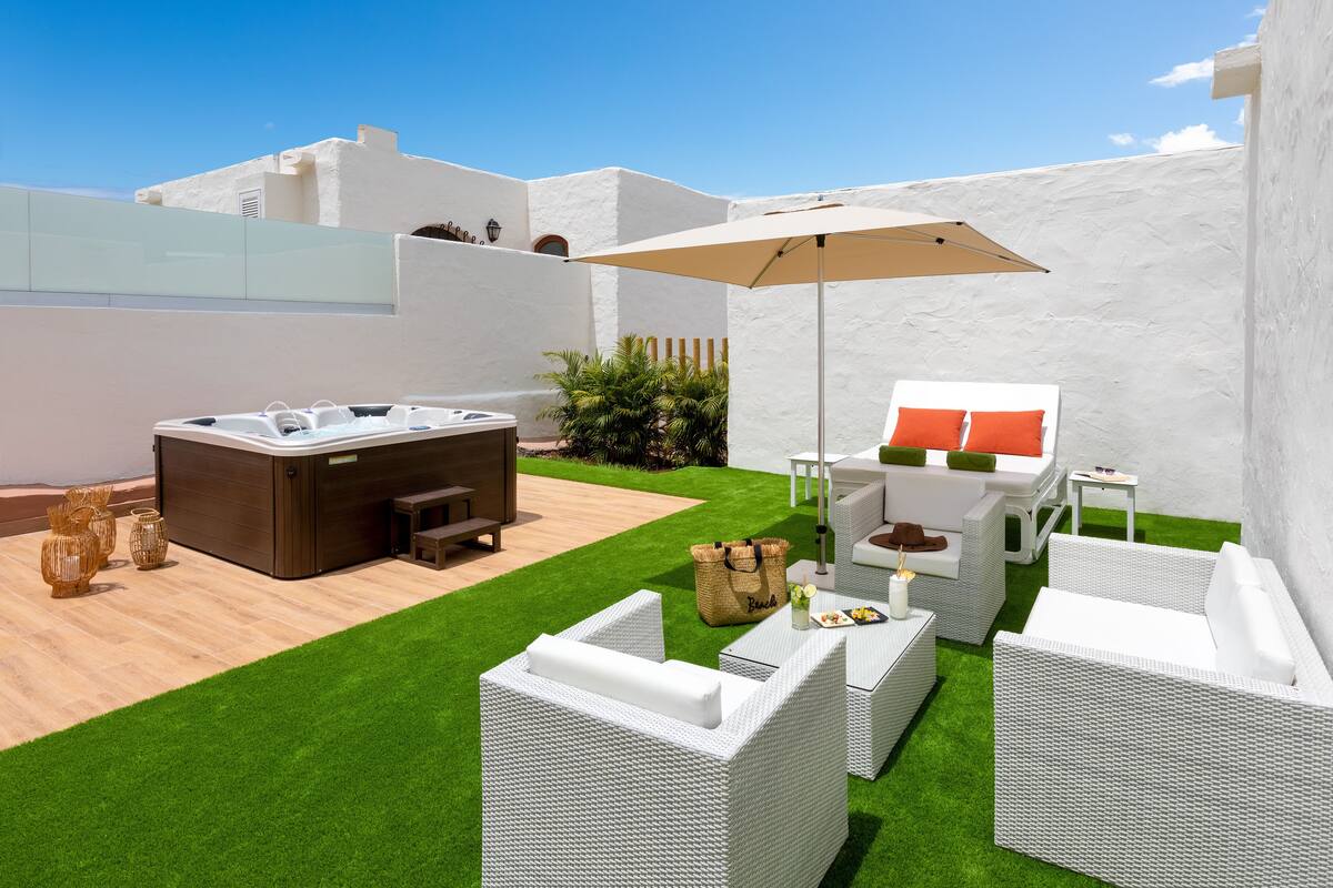 Un espace patio doté d’un jacuzzi, de meubles en osier blancs et d’un grand parasol.