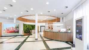 A modern hotel reception area with a central column, a reception desk, and a large digital screen displaying the hotel name. - HD Parque Cristobal Tenerife (Arona)