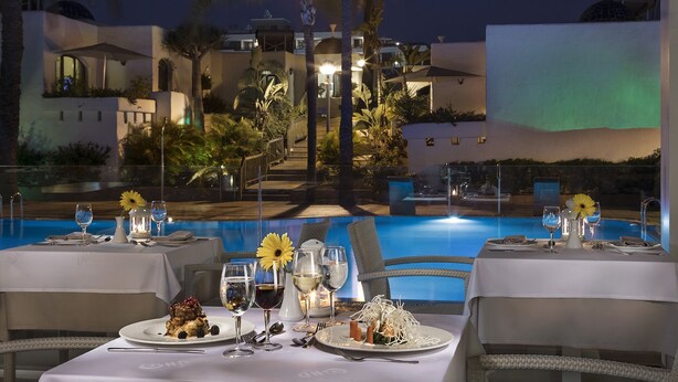 A dining area with tables set for a meal, overlooking a pool and a building with a dome roof. - HD Parque Cristobal Tenerife (Arona)