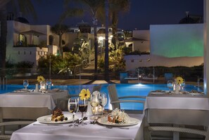 Comedor con mesas dispuestas para una comida, con vistas a una piscina y un edificio con techo abovedado.