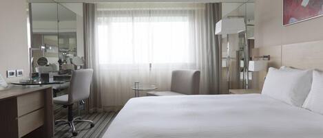Une chambre d’hôtel avec un grand lit, un bureau avec une chaise, une petite table et un miroir.