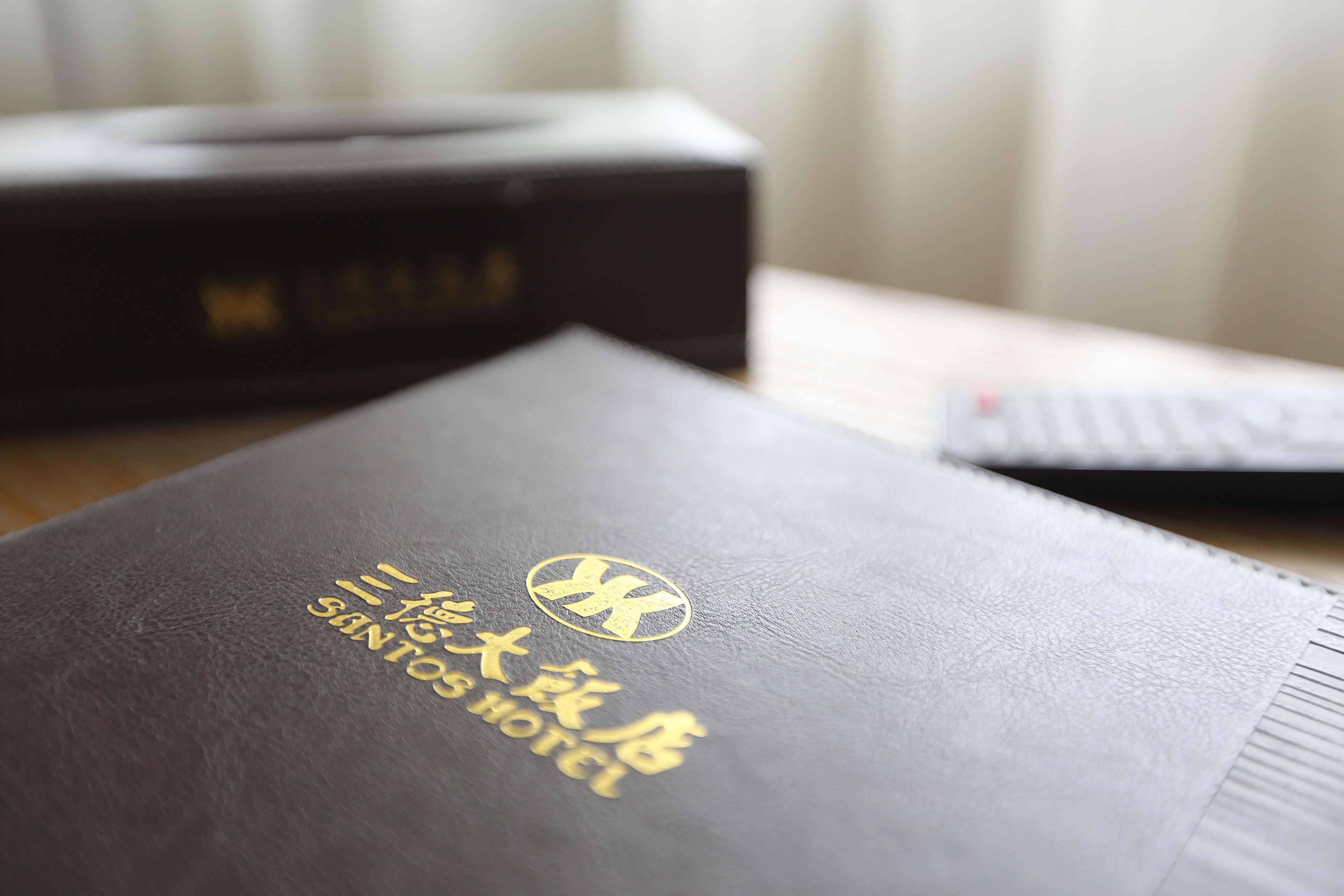 A black leather-bound book with gold embossed text and a logo, placed on a wooden surface.