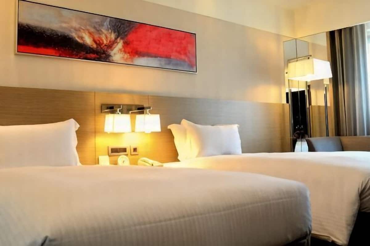 A hotel room with two beds, a large painting, a mirror, and a lamp.
