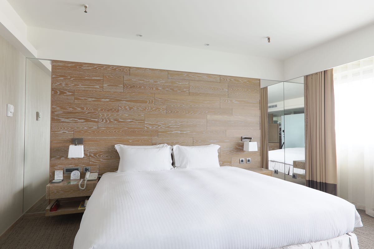 A modern hotel room with a large bed, wooden headboard, bedside tables with phones, and a mirror.