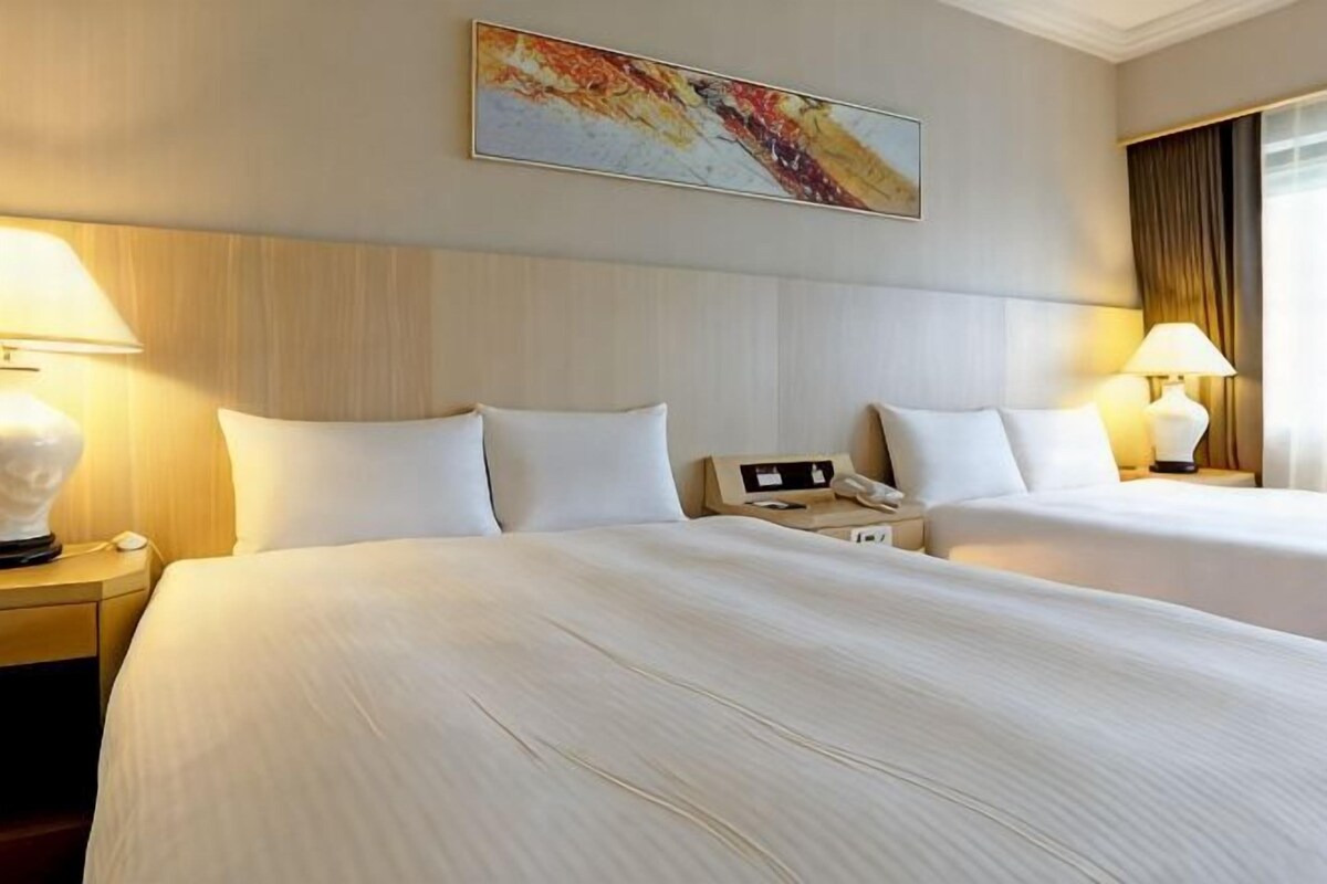 Habitación de hotel con dos camas, una mesita de noche con lámpara, teléfono y un cuadro en la pared.
