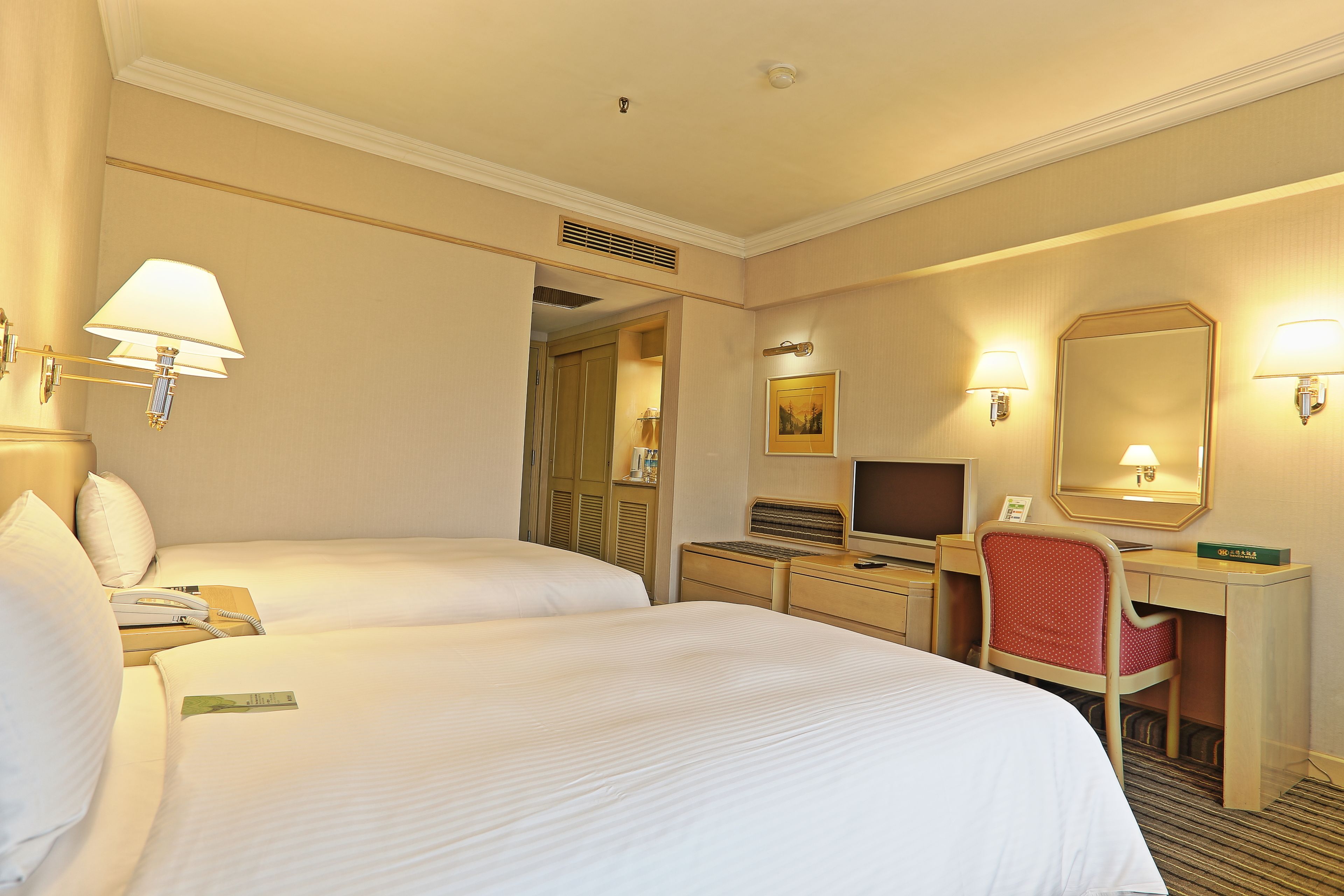 Une chambre d’hôtel avec deux lits, un bureau avec un ordinateur, une chaise et un miroir.
