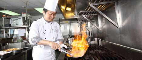 A chef cooking with flames on a grill in a professional kitchen.
