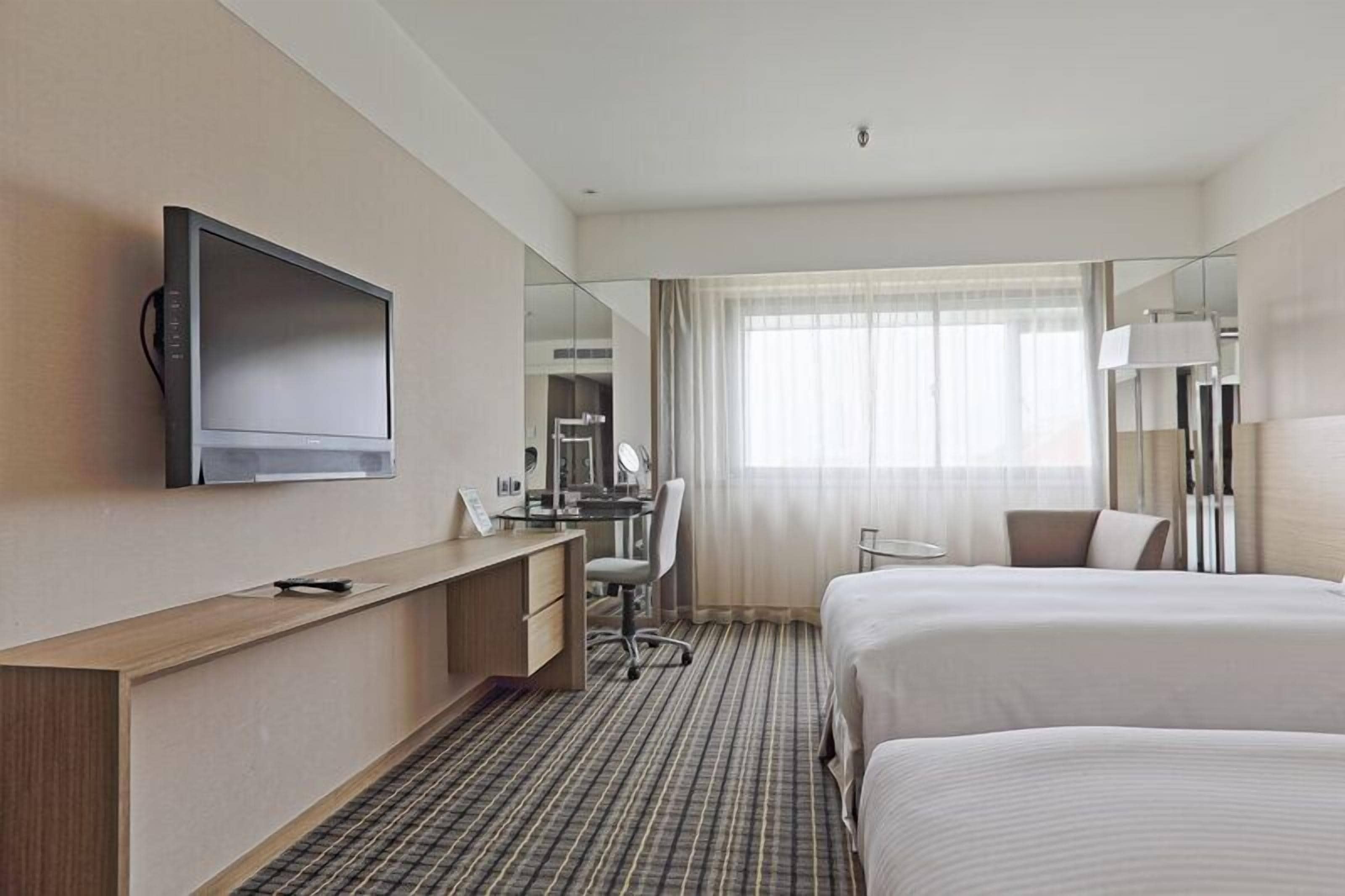 A hotel room with a bed, a desk, a television, a mirror, and a window with curtains.