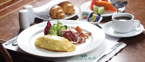 Een ontbijttafel met croissants, een omelet, spek, groenten en een kop koffie.