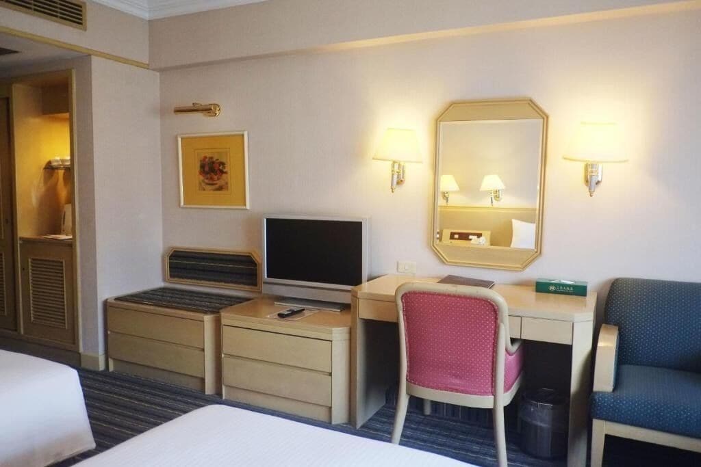 A hotel room with a bed, a desk with a computer, a chair, a mirror, and a lamp.
