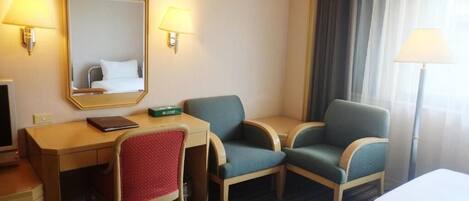A hotel room with a desk, two chairs, a bed, a mirror, and two wall lamps.