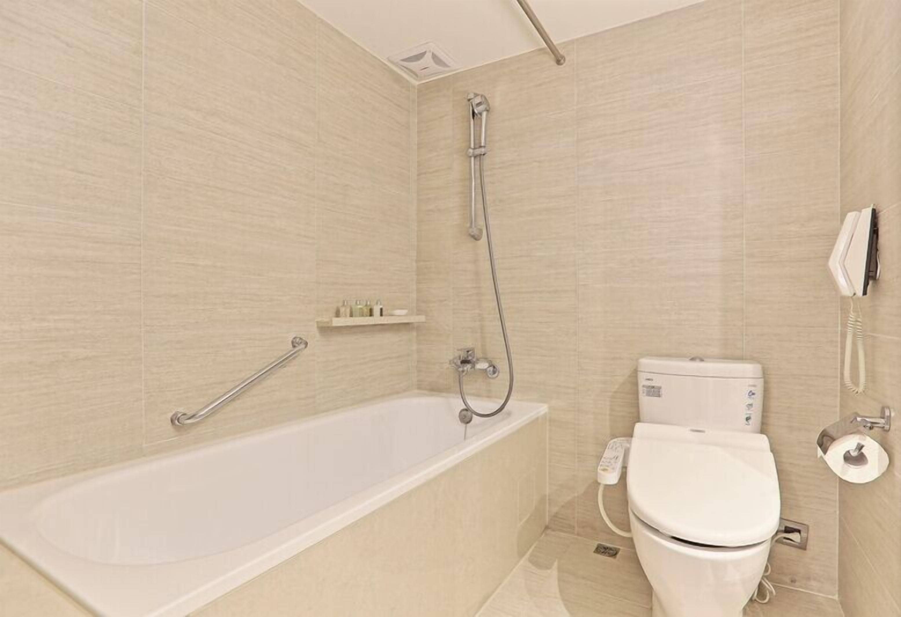 A modern bathroom with a bathtub, shower, toilet, and a hand dryer.
