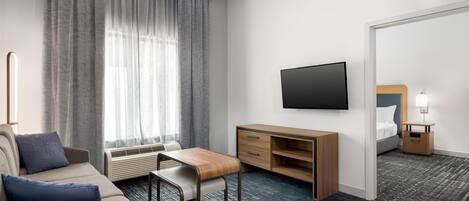 Ein Hotelzimmer mit einer Couch, einem Holztisch, einem Flachbildfernseher, einem Nachttisch mit Lampe und einem großen Spiegel.