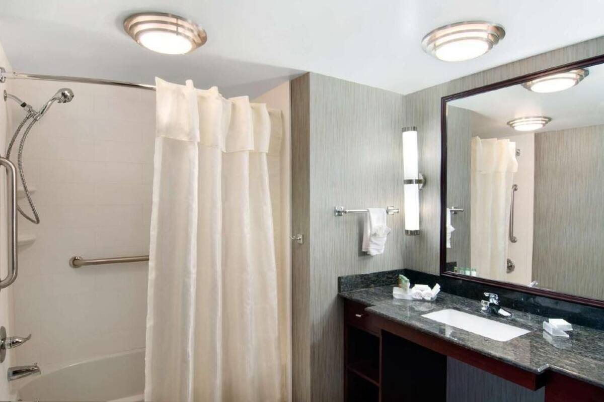 A bathroom with a shower, a sink, a mirror, and a towel rack.