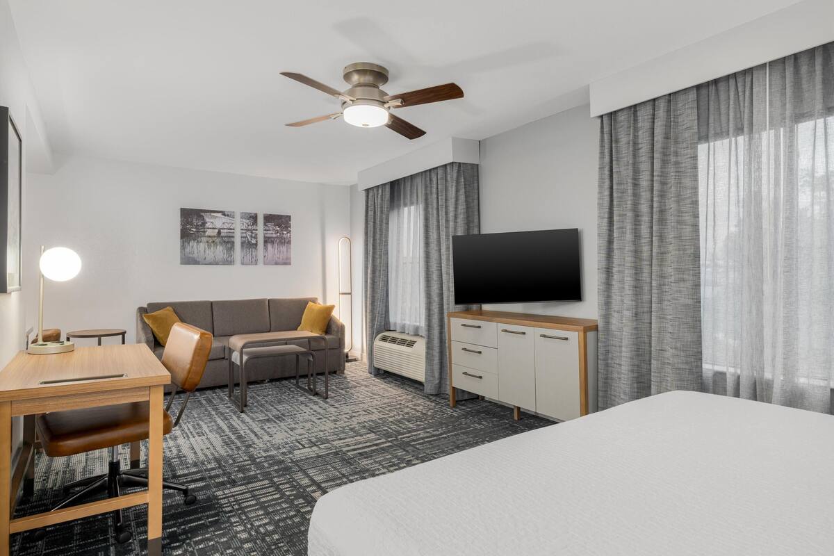 A hotel room with a bed, desk, chair, TV, and a ceiling fan.