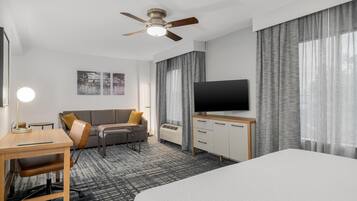 A hotel room with a bed, desk, chair, TV, and a ceiling fan.
