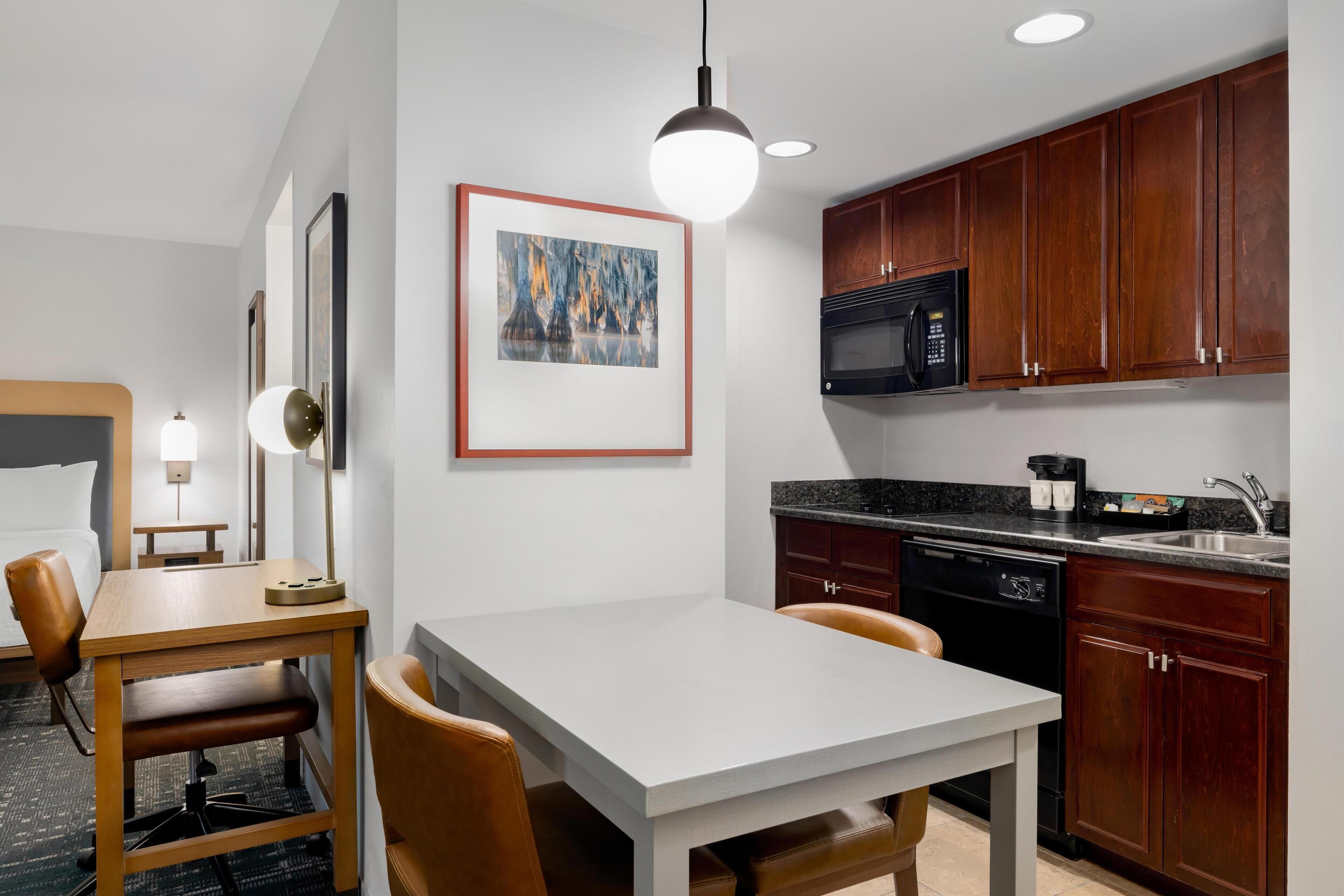 A compact hotel room with a dining area, kitchenette, and a bed.