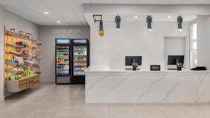 Negozio di suite alberghiere con bancone in marmo, un'unità di refrigerazione e un'ampia selezione di snack e bevande.