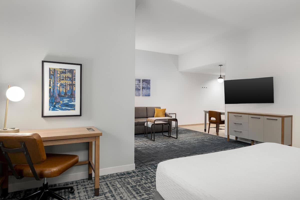 A hotel room with a bed, desk, chair, and a TV on the wall.