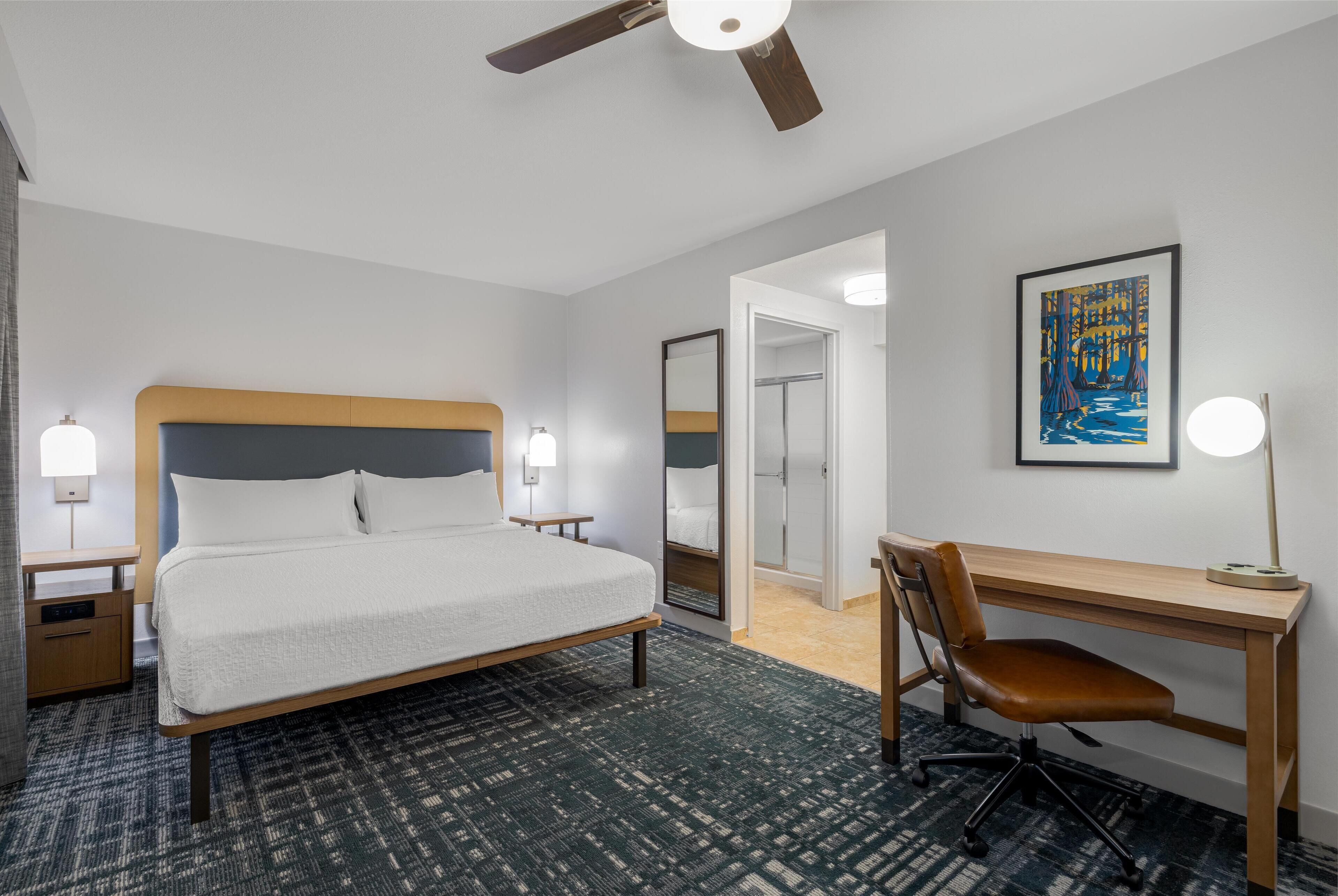 A hotel room with a bed, desk, chair, and a ceiling fan.