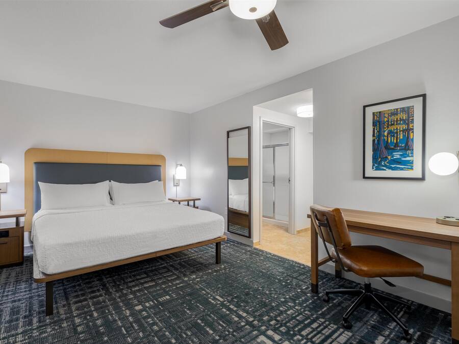 Una habitación de hotel con cama, escritorio, silla y ventilador de techo.