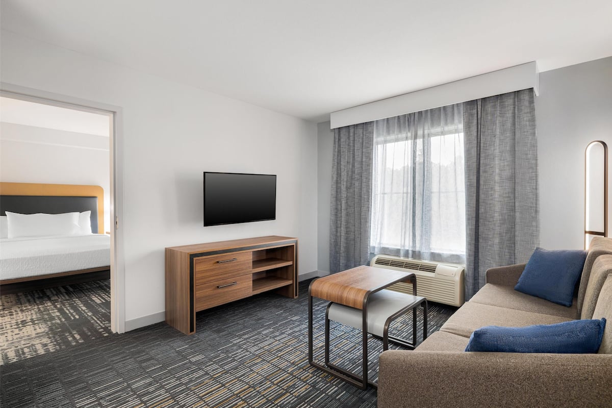 A hotel room with a bed, a TV, a sofa, a wooden cabinet, and a window with curtains.