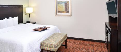 A hotel room with a bed, a bedside table with a lamp, a TV, and a patterned carpet.
