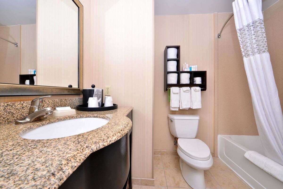 Un baño con lavamanos de encimera de granito, un espejo, inodoro y ducha con cortina.