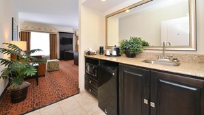 A compact hotel room with a kitchenette, a large mirror, a potted plant, and a patterned carpet. - Hampton Inn Pecos (Pecos)