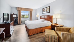 A hotel room with a bed, a desk with a television, a microwave, and a small refrigerator. There is a window with curtains, a lamp, and a framed picture on the wall. - My Hometown Inn (Mooresville)