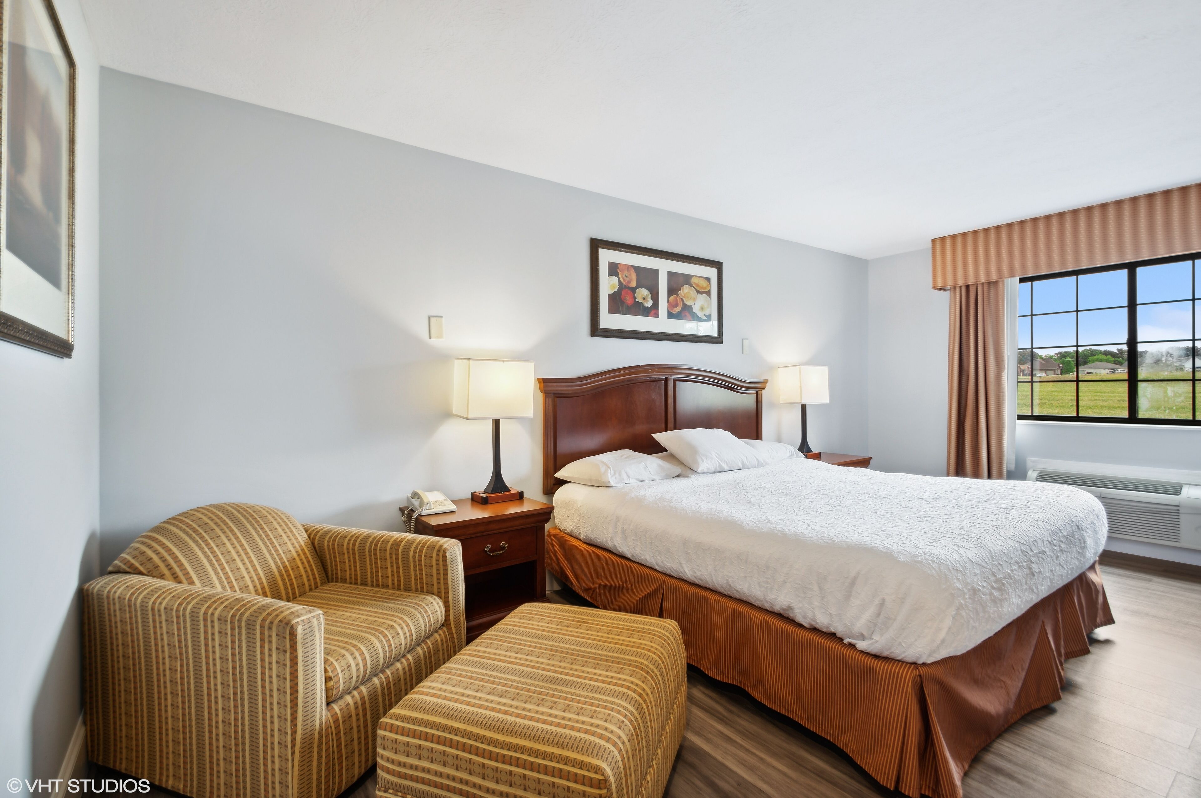 A hotel room with a large bed, two bedside tables with lamps, a sofa, and a chair.